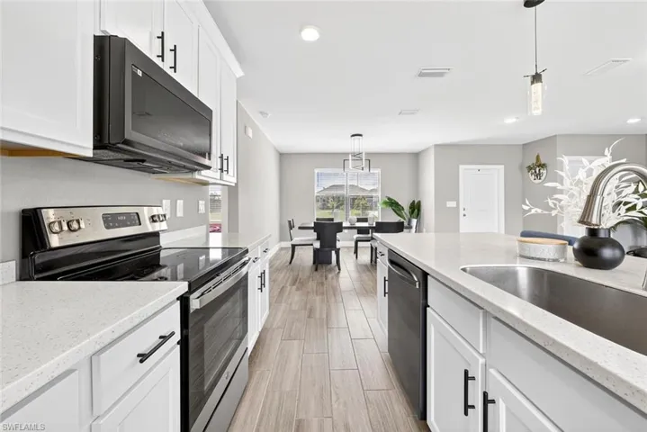 Kitchen featuring stainless steel appliances, white cabinetry, pendant lighting, light stone countertops, and recessed lighting