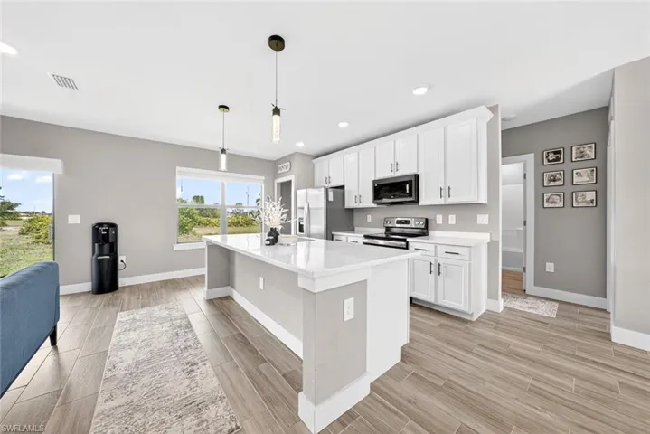 Kitchen with white cabinets, stainless steel appliances, a kitchen island with sink, wood tiled floors, and recessed lighting