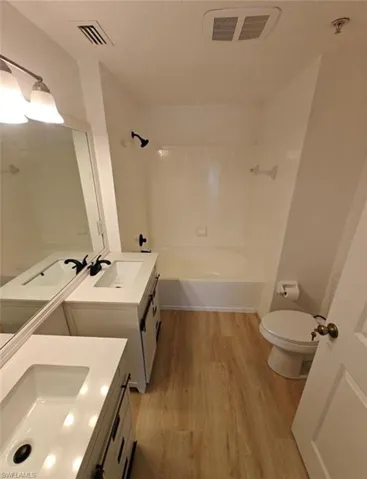 Full bath with light wood-style flooring, two vanities, and shower / bath combination