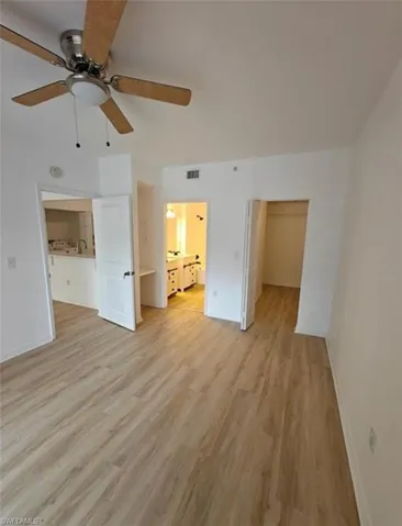 Unfurnished bedroom featuring a spacious closet, light wood finished floors, ensuite bath, and a ceiling fan