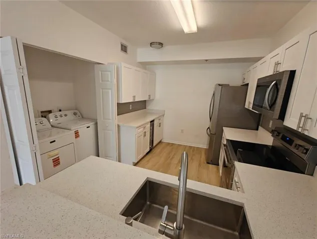 Kitchen featuring white cabinetry, stainless steel appliances, light stone countertops, light wood-style floors, and washer and dryer