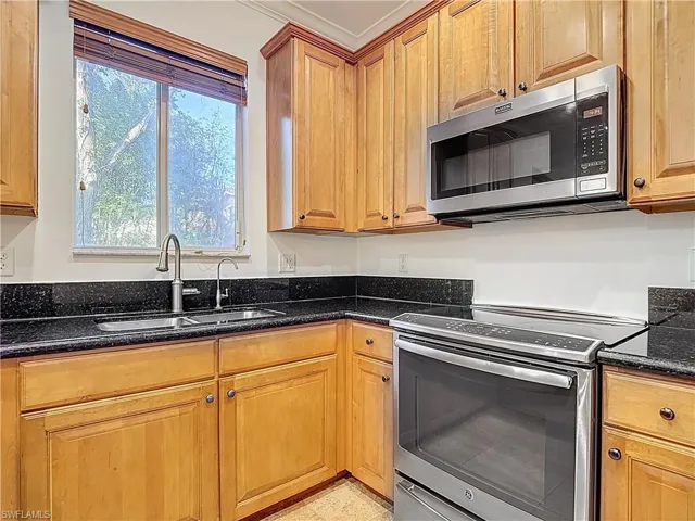 Kitchen featuring stainless steel appliances, dark stone counters, and wood finish cabinetry