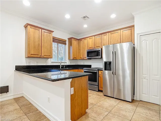 Kitchen featuring stainless steel appliances, a peninsula, dark stone countertops, crown molding, and wood finish cabinets