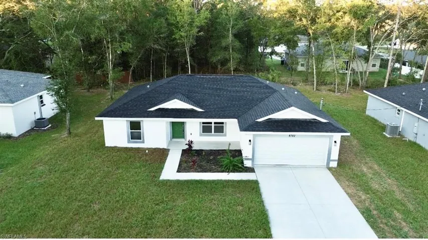 Ranch-style house featuring a shingled roof, a front lawn, an attached garage, concrete driveway, and stucco siding