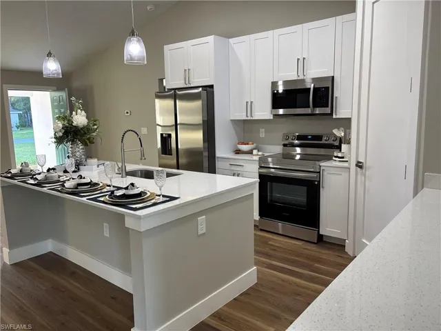 Kitchen featuring stainless steel appliances, white cabinetry, hanging light fixtures, light stone countertops, and lofted ceiling