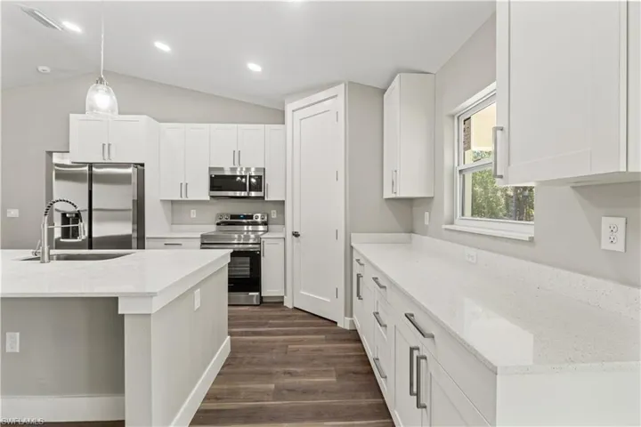 Kitchen with appliances with stainless steel finishes, decorative light fixtures, white cabinetry, light stone counters, and vaulted ceiling