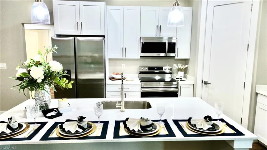 Kitchen with hanging light fixtures, appliances with stainless steel finishes, white cabinets, and light stone countertops