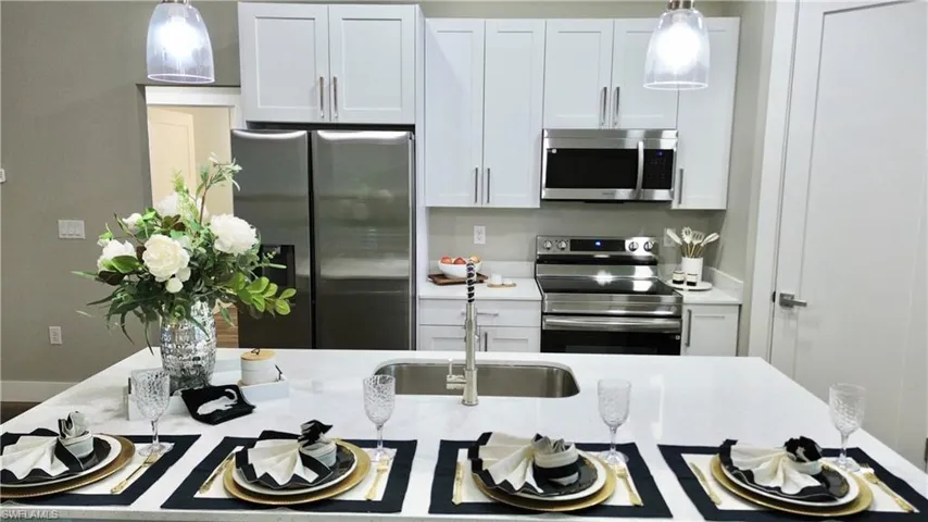 Kitchen featuring appliances with stainless steel finishes, decorative light fixtures, light stone countertops, and white cabinets