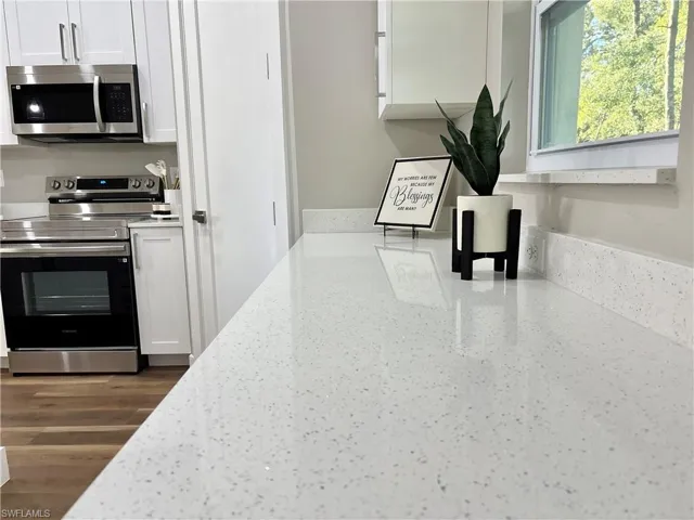 Kitchen with white cabinetry, appliances with stainless steel finishes, light stone countertops, and dark wood-type flooring