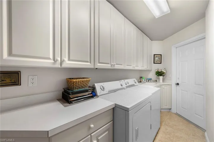 Laundry room featuring separate washer and dryer, light tile flooring, and cabinets