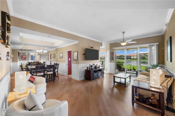 Living room with a raised ceiling, hardwood / wood-style floors, crown molding, and ceiling fan with notable chandelier
