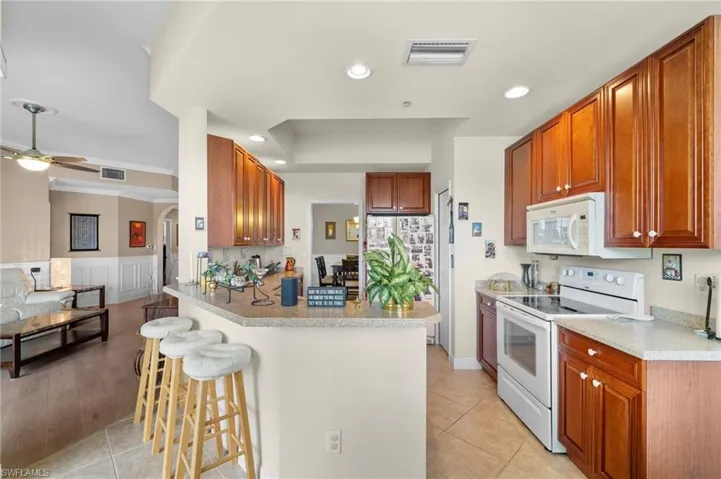 Kitchen with ceiling fan, white appliances, light tile floors, and a breakfast bar