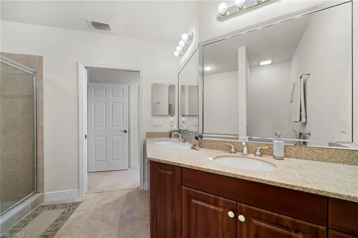 Bathroom with a shower with shower door, tile floors, double sink, and vanity with extensive cabinet space