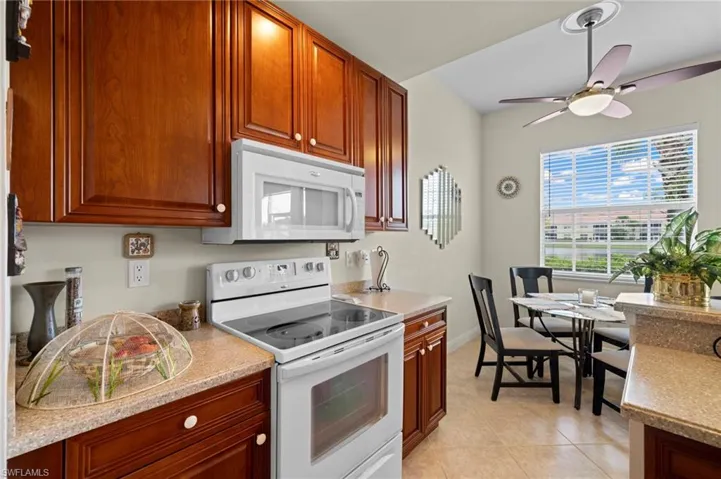 Kitchen with ceiling fan, white appliances, and light tile floors