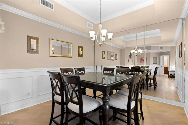 Dining room featuring a raised ceiling, an inviting chandelier, light wood-type flooring, and ornamental molding