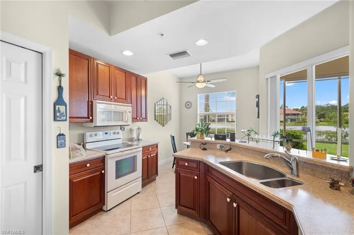 Kitchen featuring white appliances, sink, ceiling fan, and light tile floors