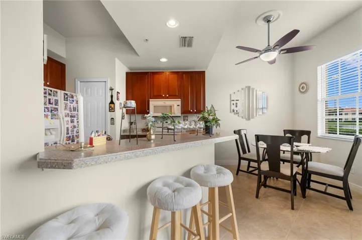 Kitchen featuring a kitchen breakfast bar, white appliances, kitchen peninsula, ceiling fan, and light tile floors