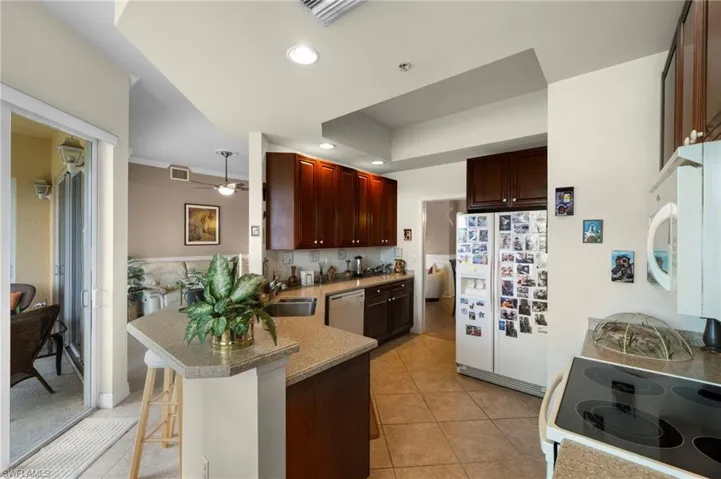 Kitchen with ceiling fan, white appliances, light tile flooring, sink, and a kitchen bar