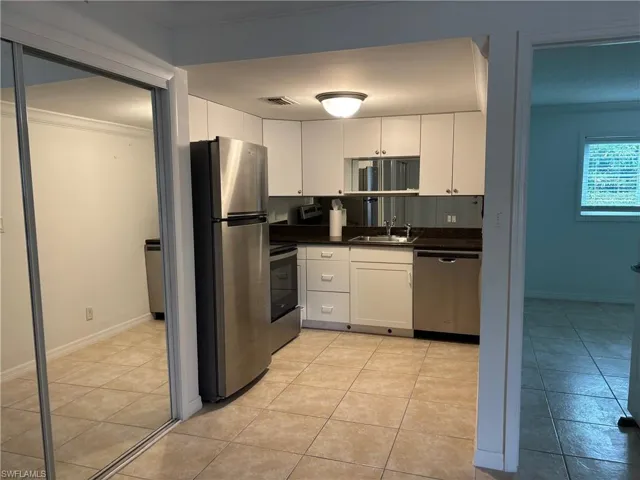 Kitchen with appliances with stainless steel finishes, ornamental molding, sink, light tile patterned floors, and white cabinetry