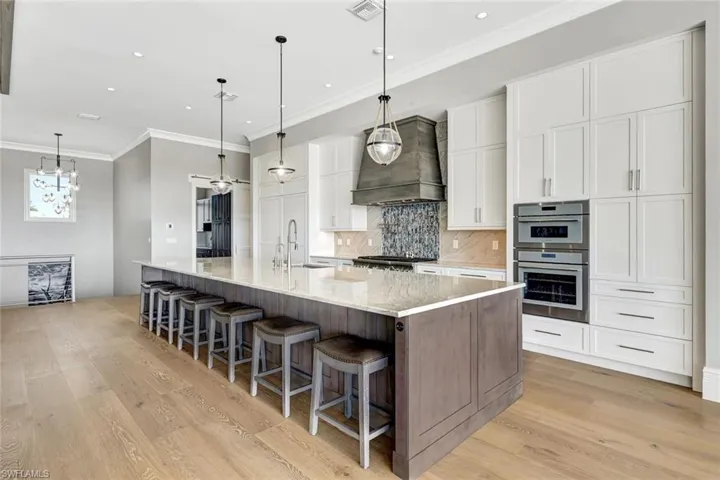 Kitchen with custom exhaust hood, crown molding, white cabinets, light wood-type flooring, and tasteful backsplash