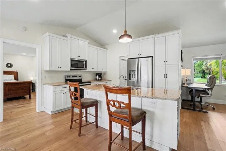 Kitchen featuring white cabinetry, stainless steel appliances, granite countertops, and wood-finish flooring