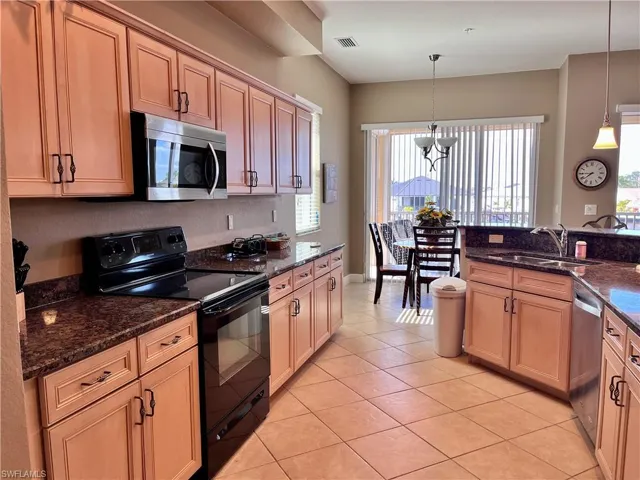 Kitchen with appliances with stainless steel finishes, light tile patterned floors, dark stone counters, and pendant lighting
