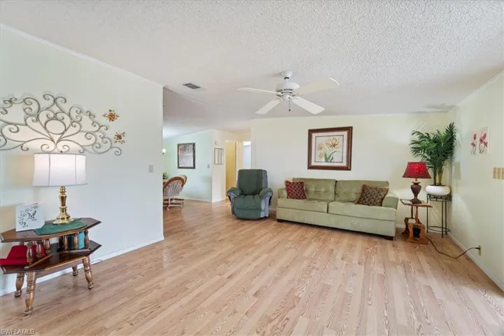Living room with ceiling fan, a textured ceiling, and light hardwood / wood-style flooring