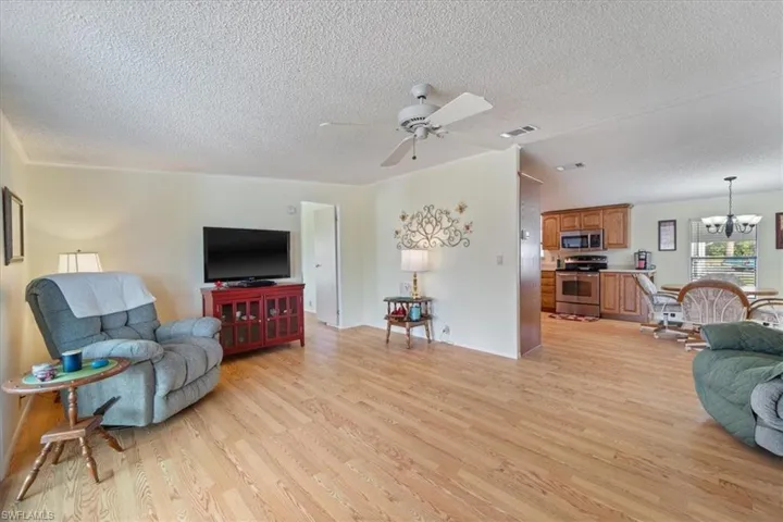 Living room featuring ceiling fan with notable chandelier, light hardwood / wood-style floors, and a textured ceiling
