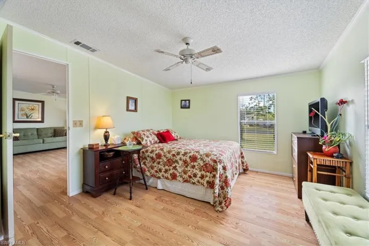 Bedroom featuring ornamental molding, ceiling fan, a textured ceiling, and light wood-type flooring