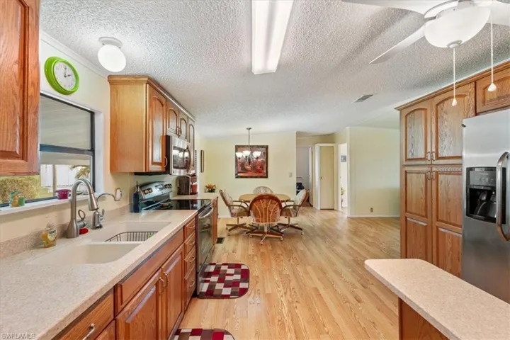 Kitchen featuring sink, hanging light fixtures, stainless steel appliances, light hardwood / wood-style floors, and a textured ceiling