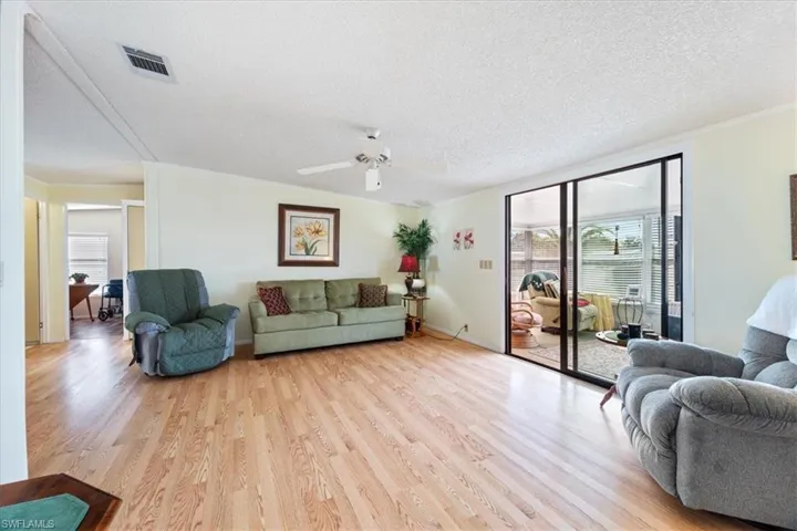 Living room with ceiling fan, a textured ceiling, and light wood-type flooring