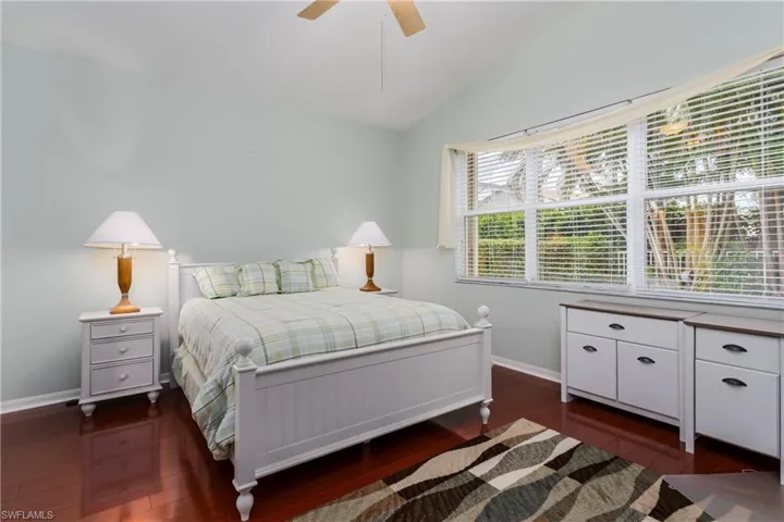 Vaulted ceiling, wood-finish flooring, multiple windows, ceiling fan, and light-toned walls