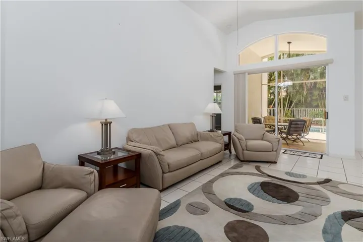 Vaulted ceiling, ceramic tile flooring, and sliding glass doors with an arched transom window opening to a screened patio with a pool
