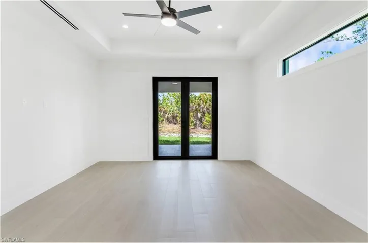 Primary bedroom with french doors, a raised ceiling, wood-look tile, ceiling fan, and recessed lighting