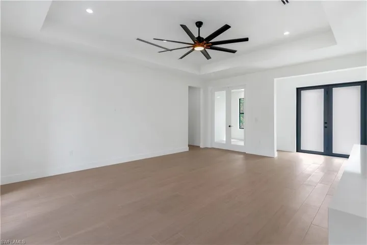Unfurnished living room with french doors, a tray ceiling, wood-look tile, a ceiling fan, and recessed lighting