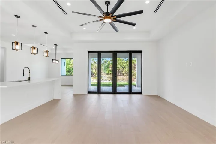 Unfurnished living room featuring healthy amount of natural light with french doors, wood-look tile, recessed lighting, a ceiling fan, and a raised ceiling