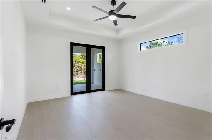 Primary bedroom featuring healthy amount of natural light, a raised ceiling, wood-look tile, and a ceiling fan