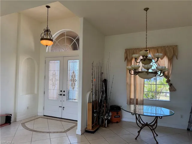 Foyer with tile patterned floors, french doors, baseboards, a notable chandelier, and a high ceiling