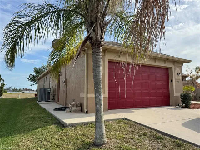 View of side of home with stucco siding, driveway, central air condition unit, and a yard