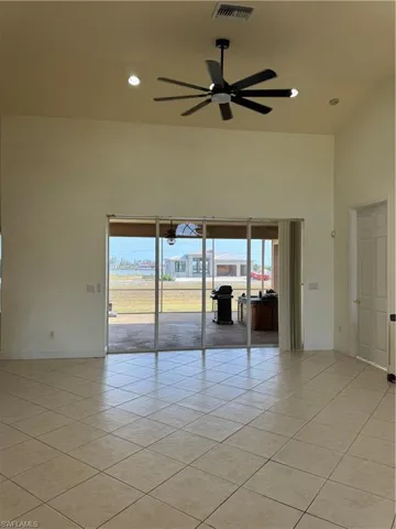 Spare room with a towering ceiling, visible vents, light tile patterned floors, baseboards, and ceiling fan