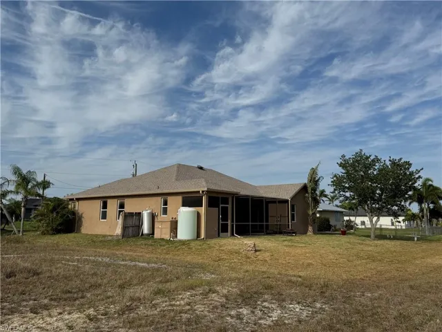 Rear view of house featuring a lawn, a shingled roof, a sunroom, and stucco siding