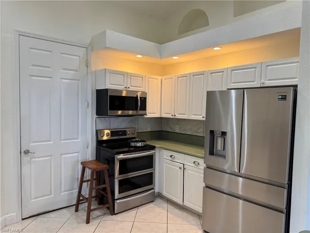 Kitchen with white cabinets, appliances with stainless steel finishes, decorative backsplash, and light tile patterned floors
