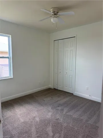 Unfurnished bedroom with dark carpet, ceiling fan, baseboards, and a closet