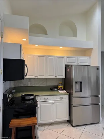 Kitchen with white cabinets, light tile patterned floors, range, and fridge