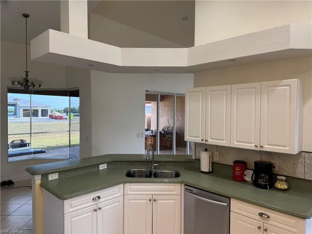 Kitchen with stainless steel dishwasher, dark countertops, a sink, white cabinets, and a peninsula