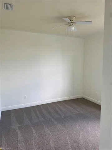 Spare room featuring dark carpet, visible vents, a ceiling fan, and baseboards