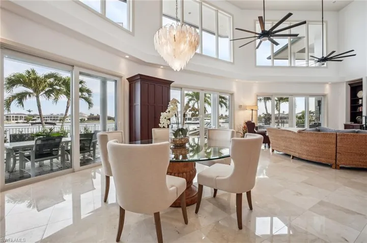 Dining area featuring a high ceiling, a chandelier, a ceiling fan, and light marble finish floors