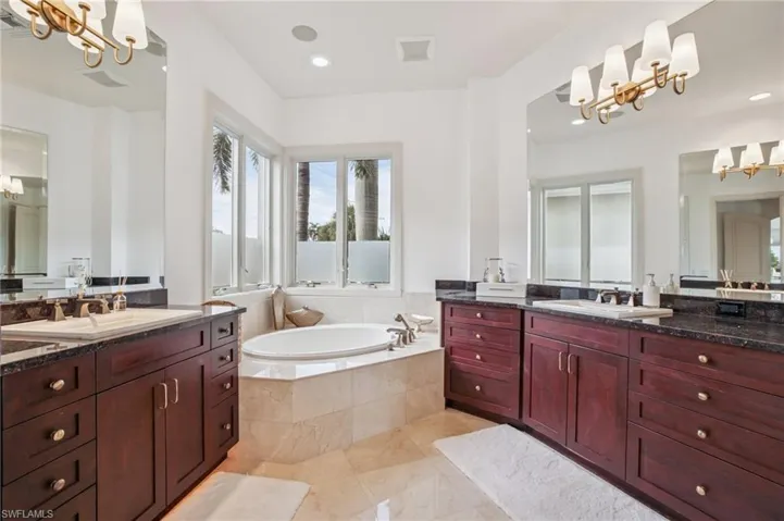 Full bath with a chandelier, a bath, two vanities, and recessed lighting