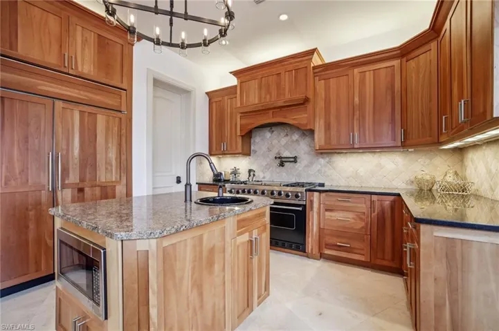 Kitchen featuring dark stone countertops, an island with sink, built in appliances, backsplash, and recessed lighting