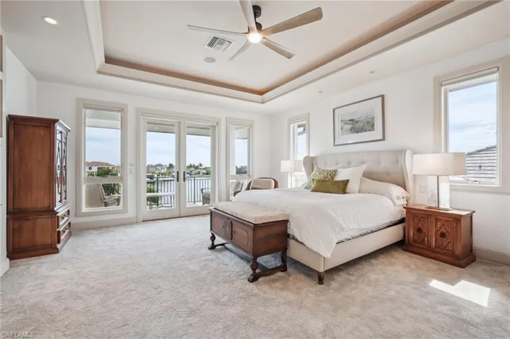 Bedroom featuring a raised ceiling, light carpet, access to exterior, and ceiling fan
